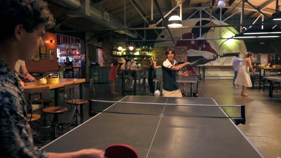 A man engaged in a game of ping pong inside a lively room setting.