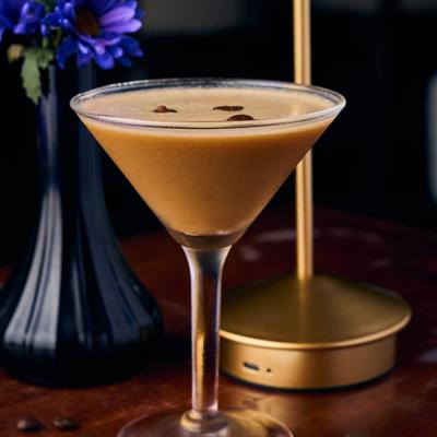 An espresso martini cocktail stands in a classic martini glass on a wooden table.