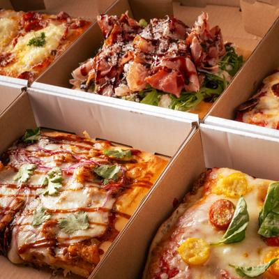 Square-cut pizza slices in open cardboard takeout boxes.