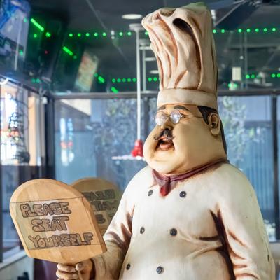 Whimsical statue of a chef holding a sign thet reads Please seat yourself.