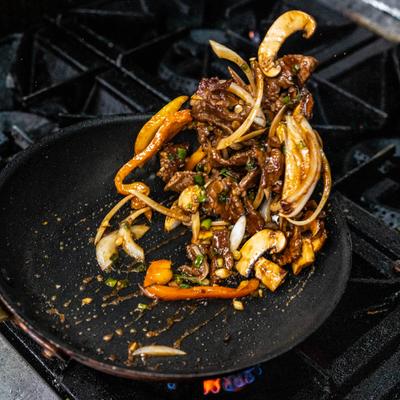 Thinly sliced beef, onions, mushrooms, and peppers stir-frying in a hot skillet.