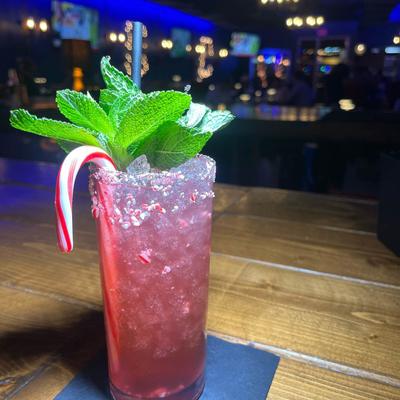 A pink mixed drink. with mint leaves and candy cane cocktail garnish.