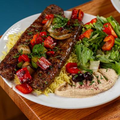 Beef kebab platter with seasoned rice, fresh green salad, and hummus.