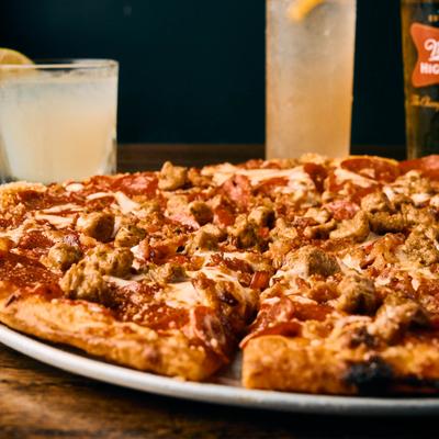 Meat lovers pizza on a round tray with hazy cocktails in the background.