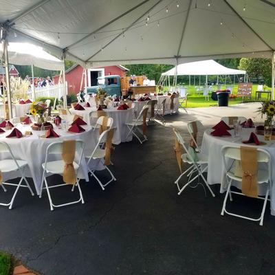 Outdoor event setup with multiple set tables with chairs, under the tent.