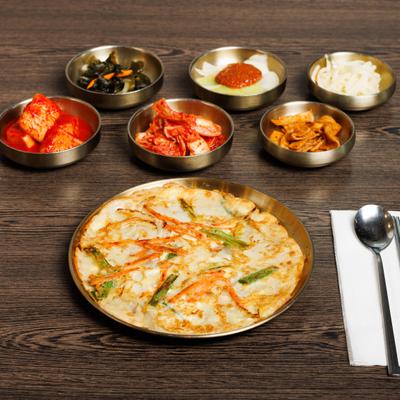 Korean-style pancake with vegetables, served alongside various small side dishes.