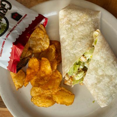 Chicken Caesar wrap served with crispy potato chips on a white plate.