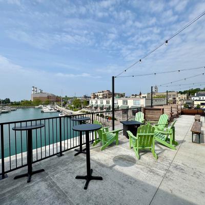 Waterfront rooftop patio with green chairs and high black tables.