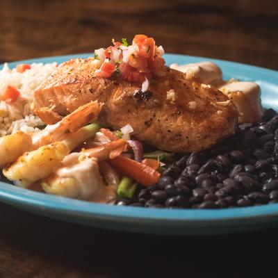 A dish with scallops, shrimp and fish, with black beans and rice on the side