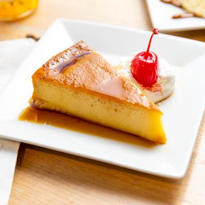 A piece of flan cake served on a plate with a cherry