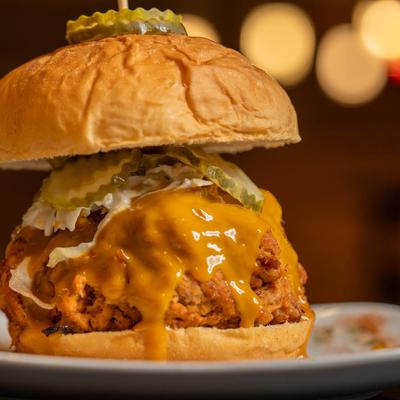 Close-up of a savory sandwich with  melted cheese, fried chicken, pickles, and slaw.