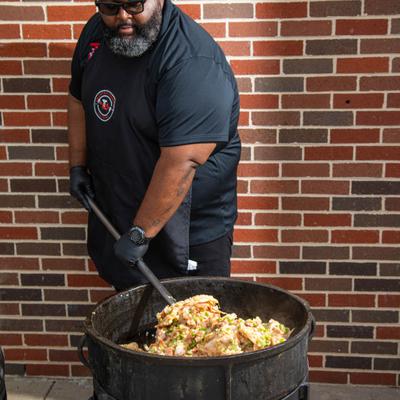 Cook stirring a large pot of seasoned meat.
