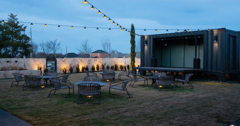 Outdoor seating area with string lights, metal furniture, and a container structure at dusk