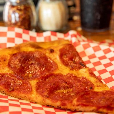 A close up of pepperoni pizza slice on a red checkered paper.