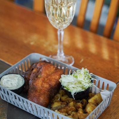 Beer-battered fried fish with tartare sauce, slaw, seasoned potatoes, and a glass of wine.