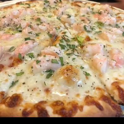 Close-up of a shrimp pizza topped with melted cheese, fresh herbs, and black pepper.