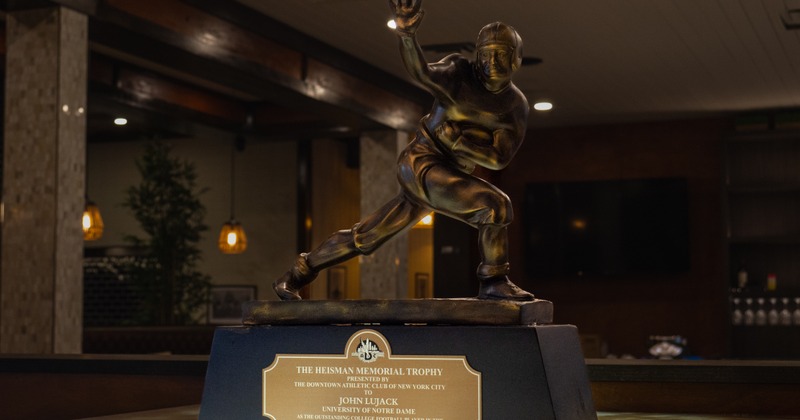 A bronze statue of a football player, representing the Heisman Trophy, sits prominently indoors