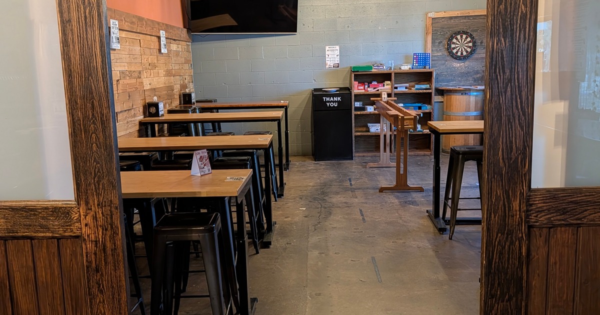 Private event room with high-top tables, TV, dartboard, games, and rustic décor for gatherings and meetings.