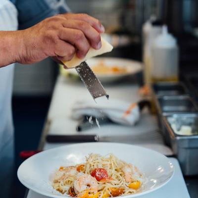 Kitchen area, kitchen staff member grating parmesan on a dish