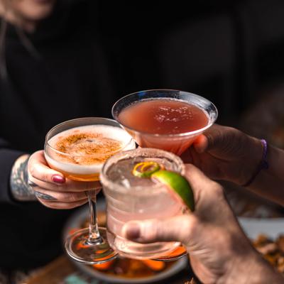 Three people clinging glasses with cocktails over the table.
