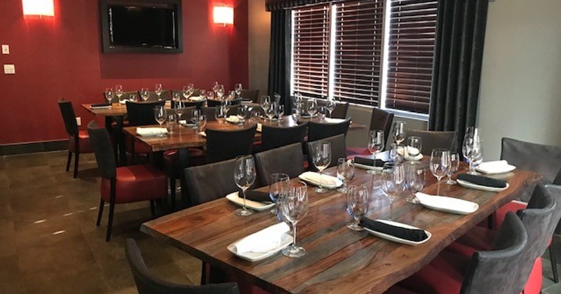 Dining area with wooden tables, neatly set with glasses, napkins, and cutlery