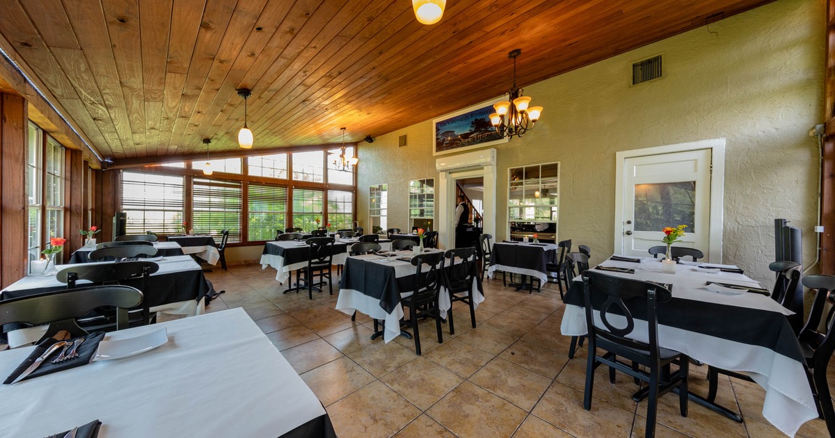 Interior, dining room with tablecloths on tables, place settings, and floral display