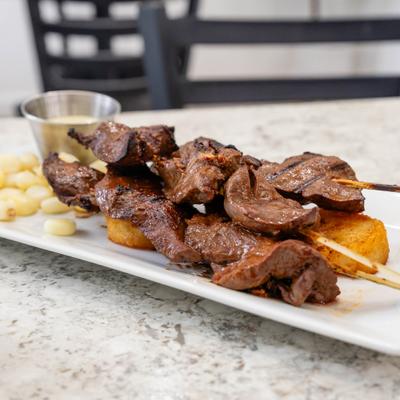Grilled beef heart skewers served with potatoes and Peruvian corn.