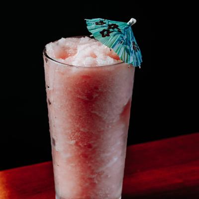 Frozen pink cocktail in a tall glass with paper umbrella garnish.