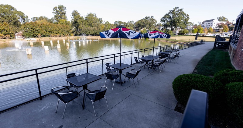 Outdoor seating area with tables and umbrellas by a pond with fountains