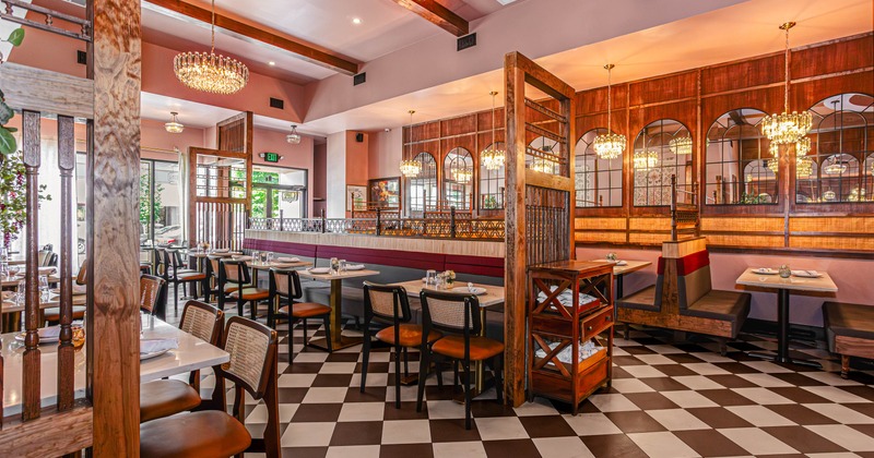 Elegant interior - checkered flooring, wooden tables, chandeliers and arched mirrors lining the wall
