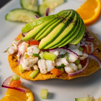 Shrimp tostada with avocado slices and orange garnish.