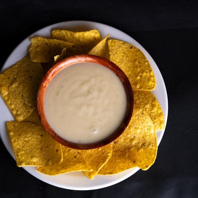 Queso dip and chips on a white plate atop a dark table.