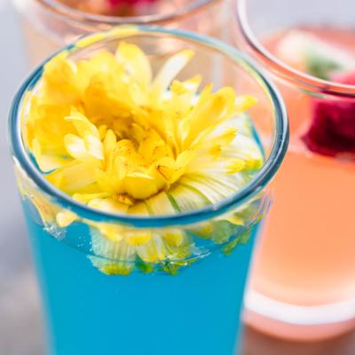 Blue cocktail garnished with a yellow flower.