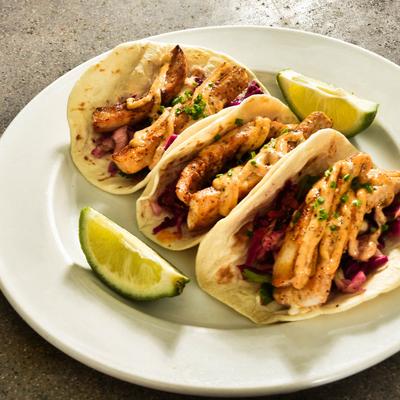 Fresh Baja Fish Tacos served on a white plate with two lime wedges.