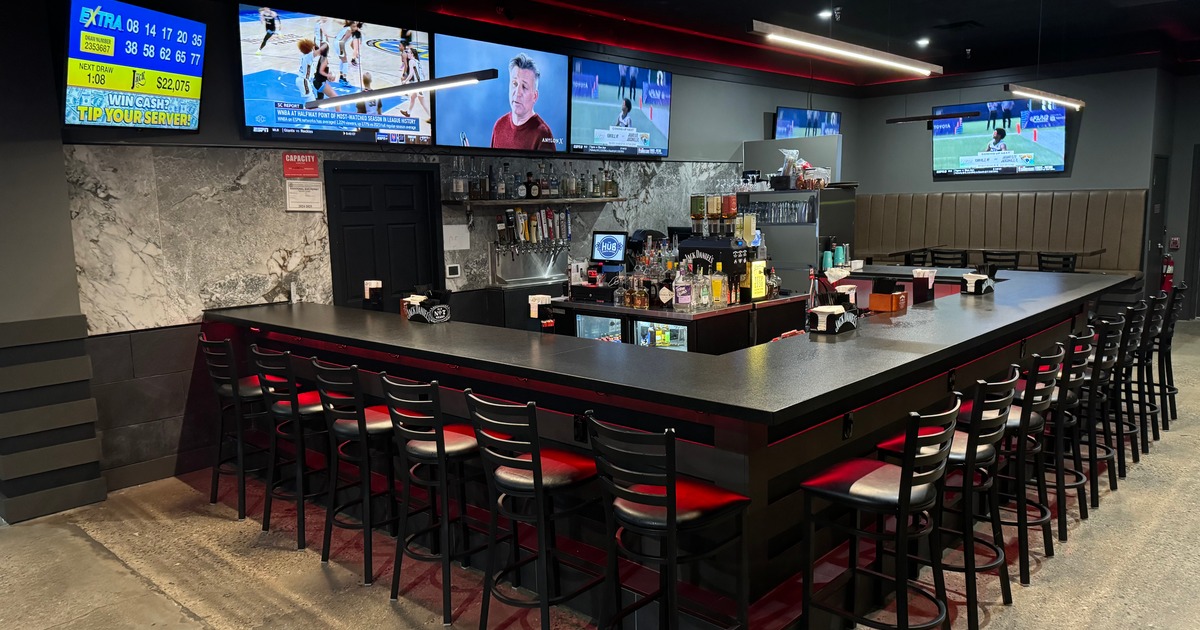 Bar area with stools, liquor bottles, and multiple TVs playing sports