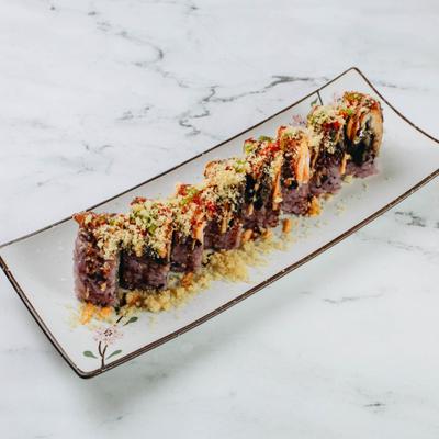 Sushi roll coated with toppings on rectangular plate.