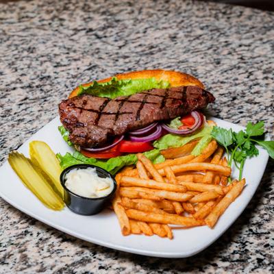 Steak sandwich served with fries, sliced pickles and a dipping sauce.
