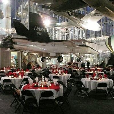 Banquet event with dining tables beneath suspended airplanes in an aviation museum.