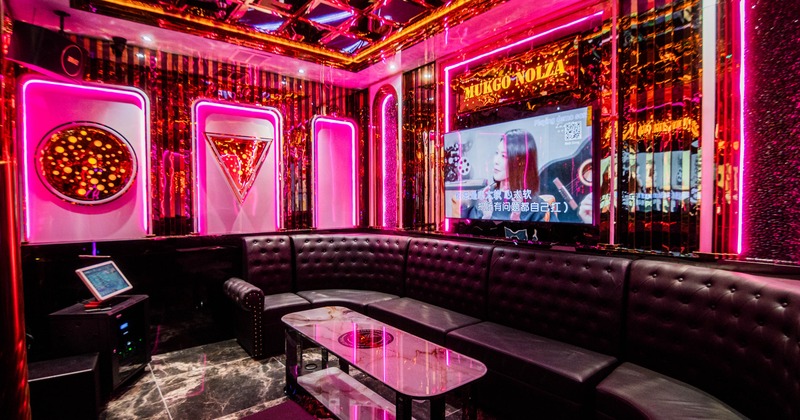 Interior, karaoke room, pink neon lighting, large leather sheeted sofa, karaoke machine