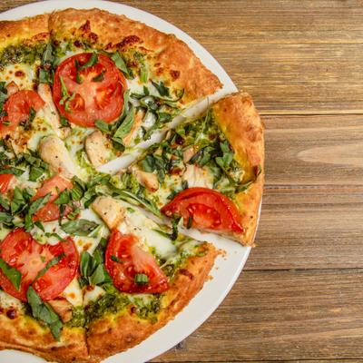 Pizza with tomato, grilled chicken, basil and pesto on a wooden table