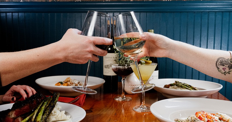 2 hand with 2 glasses with wine, toasting above diner table