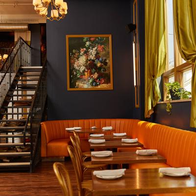 Wooden tables lined up along orange banquette bench with framed art.