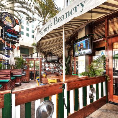 Outdoor seating area at Barney's Beanery with rustic decor, leafy plants, and a TV screen