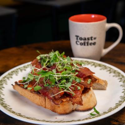 BLT toast with smoked bacon and microgreens next to a branded mug.