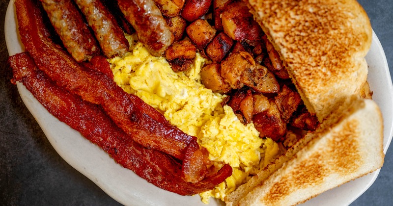 Breakfast plate wirh scambled eggs, bacon, sausage links, home fries and a toast