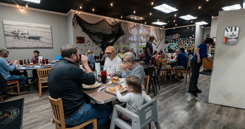Diner area, tables and chairs, wall see decoration, family in front eating
