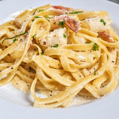 Fettuccine with creamy white sauce, cheese, herbs and pieces of meat on a white plate..