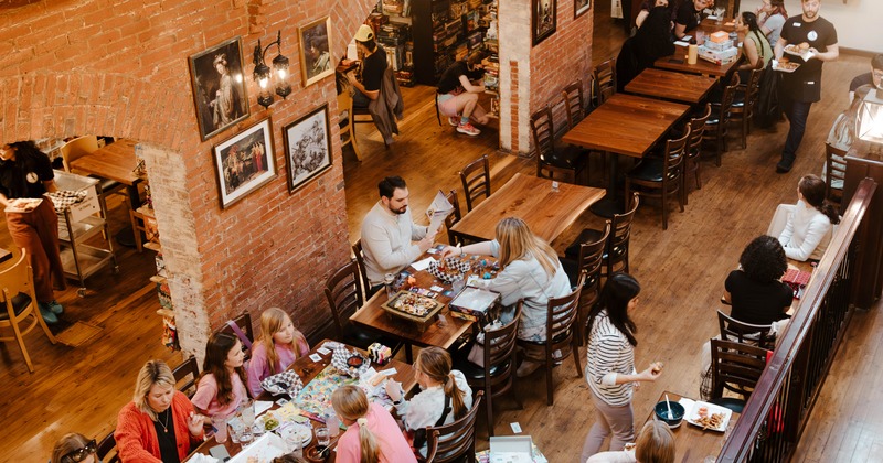 PIcture of the dining room with long wooden tables with people playing games and eating food