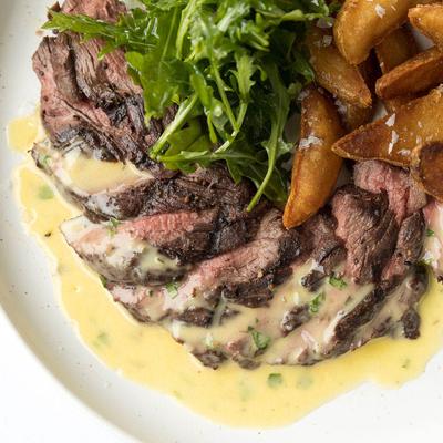 Sliced steak with golden potatoes, arugula, and creamy sauce.