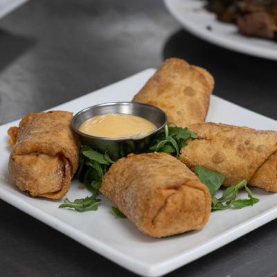 Fried egg rolls served on a square white plate with a side of dipping sauce.